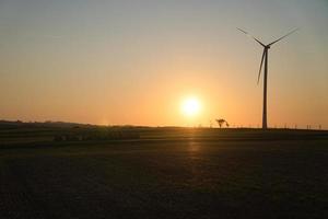 turbina eólica em uma colina em frente a um campo e à beira da floresta ao pôr do sol foto