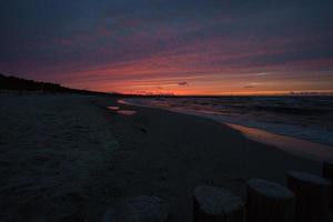 pôr do sol na costa do Báltico com nuvens roxas no céu e groynes em primeiro plano. foto