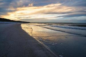 pôr do sol na costa do Báltico com nuvens no céu e reflexos na água. foto