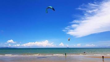 muitas pessoas jogando pipa, parasail ou pára-quedas na praia com mar ou oceano, céu azul e fundo de nuvem com espaço de cópia. conceito de atividade e esporte foto