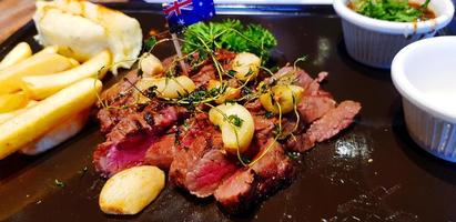 feche o bife australiano com alho frito, ervas, batatas fritas, sal e molho picante na panela ou prato quente. deliciosa refeição no prato e carne meio mal passada. foto