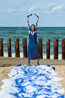 artista performática mulher feliz em vestido azul manchado com tintas guache azul dançando na praia foto