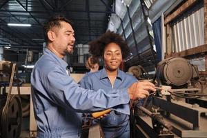 engenheiros afro-americanos asiáticos masculinos e femininos em trabalho uniforme de segurança inspecionando a corrente de tensão das máquinas, verificando e mantendo na fábrica de fabricação, ocupações de serviço do sistema elétrico. foto