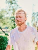 retrato de homem caucasiano, balançando a cabeça com salpicos de água. diversão de verão, festa, férias, emoções, prazer, relaxamento, conceito de refresco foto