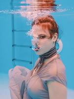 retrato de arte surreal de jovem de vestido cinza e cachecol frisado debaixo d'água na piscina foto
