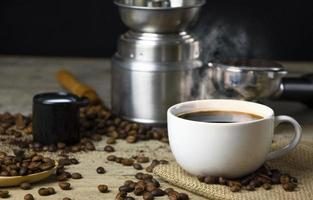 xícara de café americano preto em uma mesa de madeira com uma pilha de grãos de café arábica torrados em fundo preto. foto