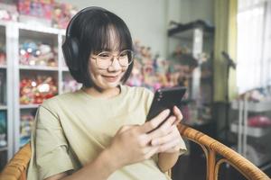 jovem mulher asiática adulta usar fone de ouvido ouvir música e relaxar usando smartphone para relaxar em casa foto
