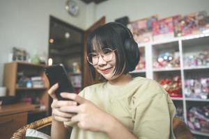 jovem mulher asiática adulta usar fone de ouvido ouvir música e relaxar usando smartphone para relaxar em casa foto