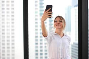 retrato de uma jovem atraente fazendo foto selfie no smartphone no fundo do prédio de escritórios moderno