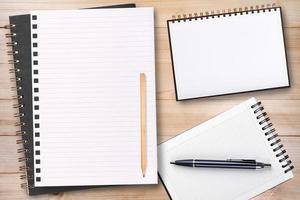 um caderno em branco aberto com lápis e caneta na mesa de madeira, modelo de negócios simulado para adicionar seu texto foto