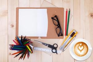 um caderno em branco aberto com lápis de cor, canetas e café na mesa de madeira foto