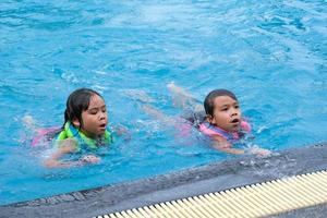 irmãzinhas felizes brincam na piscina ao ar livre do resort tropical durante as férias de verão em família. crianças aprendendo a nadar. atividades de verão saudáveis para crianças.