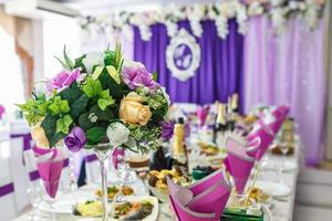 lindas flores na mesa de jantar elegante no dia do casamento. decorações servidas na mesa festiva em fundo violeta foto