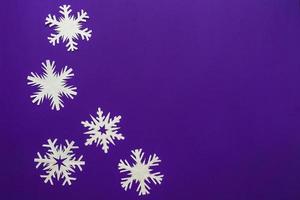 flocos de neve de papel branco diferentes formas e tamanhos em fundo violeta. vista do topo. foto