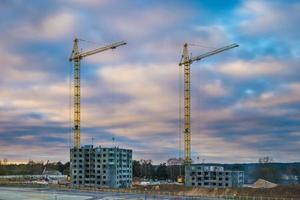 guindastes de torre de silhueta e edifícios altos de vários andares inacabados em construção em dia nublado foto