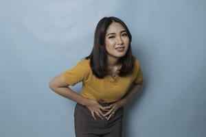 jovem mulher asiática com braços na barriga e curvando-se com expressão de dor de estômago foto
