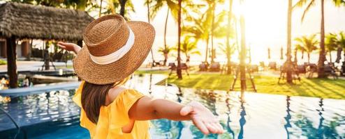 jovem viajante relaxando e apreciando o pôr do sol por uma piscina de resort tropical enquanto viaja para as férias de verão foto