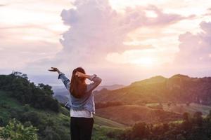 feliz jovem viajante relaxando e olhando o belo pôr do sol no topo da montanha foto