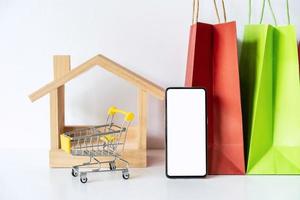 sacos de compras de papel colorido na mesa branca com telefone inteligente de tela vazia, compras on-line em casa conceito foto