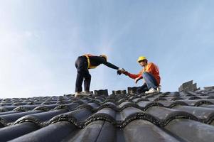 construtores em roupas de trabalho instalam novas ferramentas de cobertura, ferramentas de cobertura, furadeira elétrica e as usam em novos telhados de madeira com chapas de metal foto