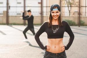 mulher de dançarina de hip hop elegante vestido preto com corrente ama e um boné. homem de pé em uma pose de dança no fundo. foto