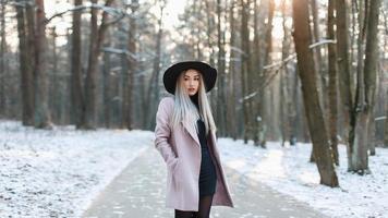 jovem mulher bonita na moda elegante chapéu e casaco de pé em um parque de inverno foto