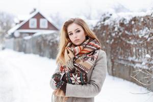 linda jovem com roupas elegantes de inverno andando perto da casa em dia de inverno foto