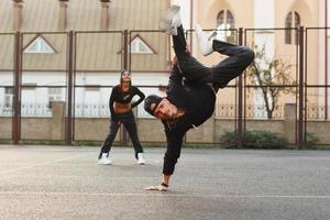 cara bonito em uma elegante roupa preta dançando hip-hop. dançarino em pé na mão dele. a garota está atrás do cara. foto