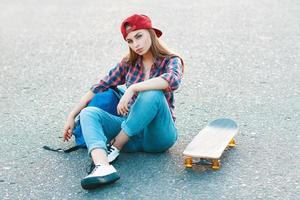 mulher jovem e bonita bonita com uma bolsa e skate sentado na calçada. foto