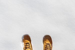 pernas humanas com botas de couro amarelo em pé na neve. vista do topo foto