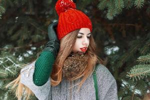 jovem elegante em um boné vermelho e suéter verde em pé no fundo de abeto foto