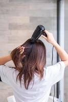 jovem usando secador de cabelo em casa ou hotel. penteados e conceitos de estilo de vida foto