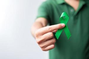 mão segurando a fita verde para fígado, vesícula biliar, ducto biliar, cervical, câncer renal e mês de conscientização do linfoma. conceito de saúde e dia mundial do câncer foto