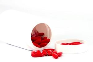 comprimidos de medicamento vermelho saindo do frasco branco