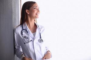 mulher médico com estetoscópio em pé perto da parede cinza foto