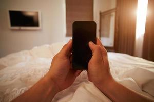 pov da pessoa na cama, olhando para o telefone móvel foto