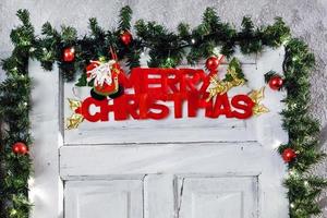 a inscrição de um feliz natal em uma porta de madeira branca, cercada por brinquedos e ramos de abeto foto