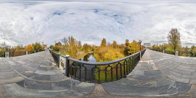 panorama completo do cubo esférico sem costura visão de ângulo de 360 graus na ponte pedonal através do pequeno rio no parque da cidade de outono em projeção equirretangular, pronto para conteúdo de realidade virtual ar vr foto