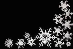 flocos de neve de papel branco diferentes formas e tamanhos em fundo preto de papelão. vista do topo. foto