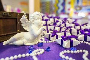 anjo de cerâmica na mesa com uma toalha de mesa violeta e pequenos presentes para convidados dos noivos foto