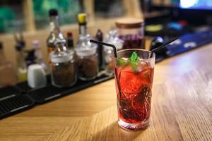 coquetel vermelho em um copo com hortelã e dois tubos em uma mesa em um bar de luxo