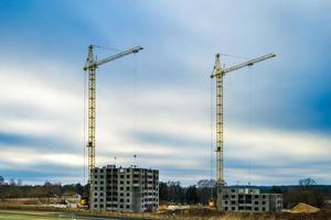 guindastes de torre e vários andares inacabados perto de edifícios em canteiro de obras em dia nublado à noite com fundo de nuvem colorida dramática foto