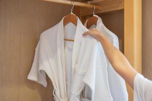 roupão de banho branco limpo pendurado no guarda-roupa de madeira no hotel de luxo ou em casa. relaxar e viajar conceito foto