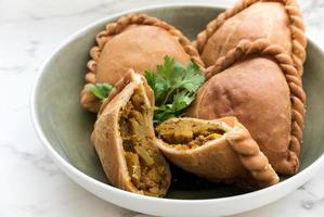 sopro de curry frito malaio ou epok-epok, comida vegetariana, isolada no fundo branco em um prato, é lanches tradicionais asiáticos que têm peles crocantes. fechar comida foto