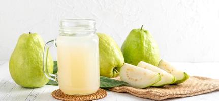 deliciosa goiaba com suco fresco em fundo de mesa de madeira branca. foto