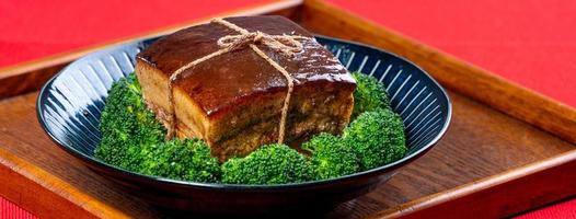 carne de porco dong po em um prato azul com brócolis com fundo vermelho. foto