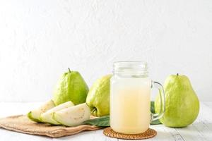 deliciosa goiaba com suco fresco em fundo de mesa de madeira branca. foto