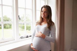retrato de mulher grávida em pé pela janela, segurando a barriga