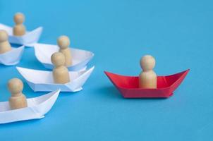 conceito de liderança - figura de madeira de pessoas no origami de navio de papel vermelho liderando o resto da figura de pessoas no navio de papel branco. copie o espaço. foto