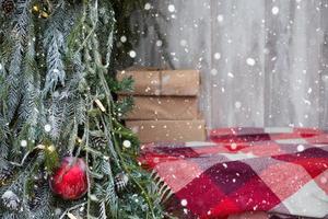 caixas com presentes para o natal em papel kraft estão em uma manta xadrez vermelha perto da árvore de natal ao ar livre. decorações de rua da cidade, neve, clima de ano novo, luzes de fadas foto